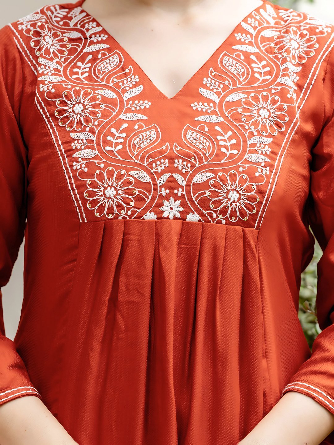 Close-up of the densely embroidered yoke in cream thread on the rust kurta